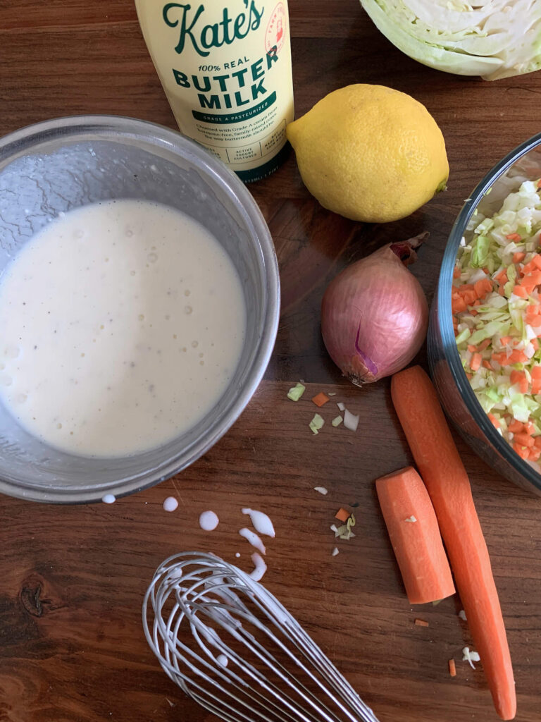 A bowl of ranch dressing with a bottle of kates buttermilk, a whisk, and some vegetables