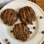 chocolate chip cookies with caramel drizzle on a plate with chocolate chips scattered around and a stick of kate's butter