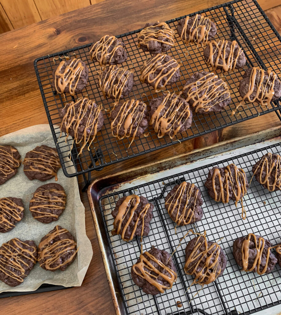 chocolate cookies with caramel drizzle on a cooling rack and cooking sheets