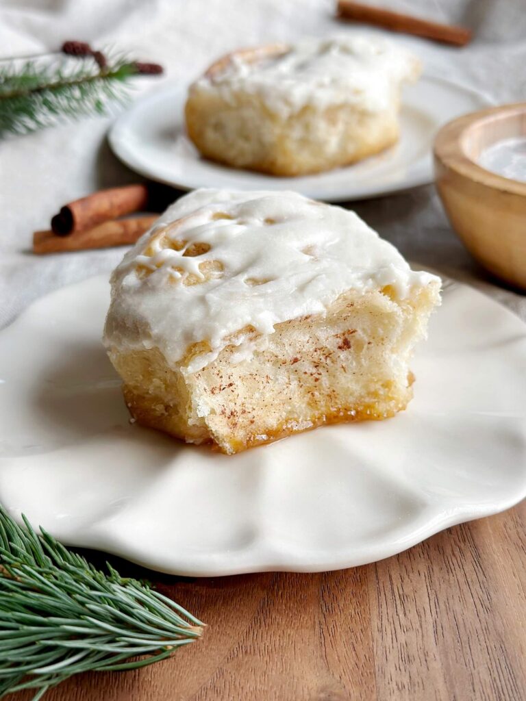 Cinnamon roll with icing on it sitting on a plate with a bite taken out of it